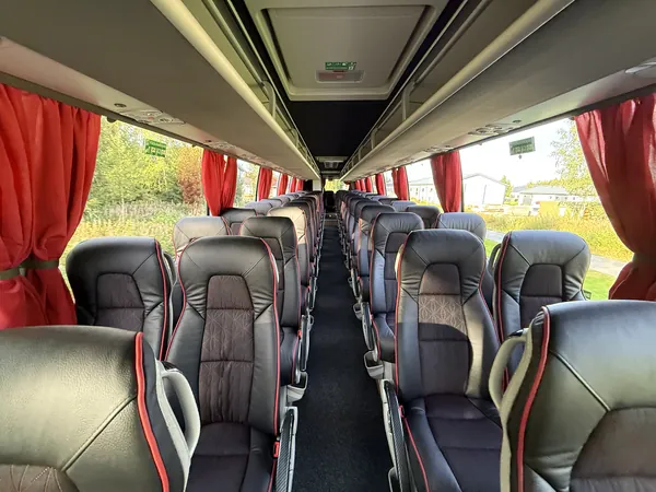 Tilausbussin matkustamo: nahkaistuimet, punaiset verhot ja keskikäytävä